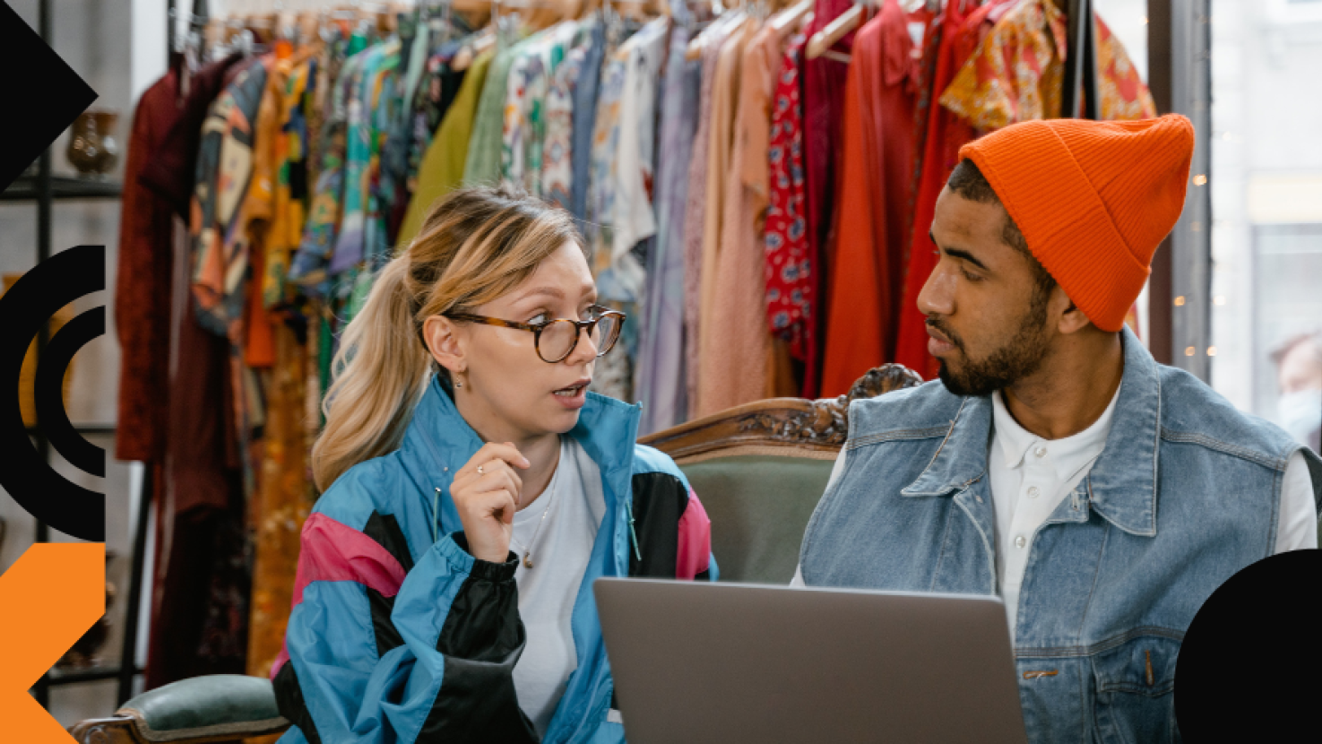 Two coworkers discussing with a line of clothing hanging behind them