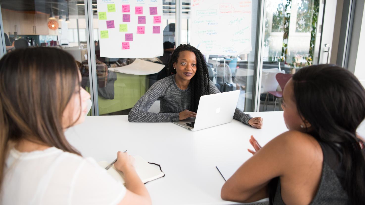 3 women discussing at a desk with their laptops